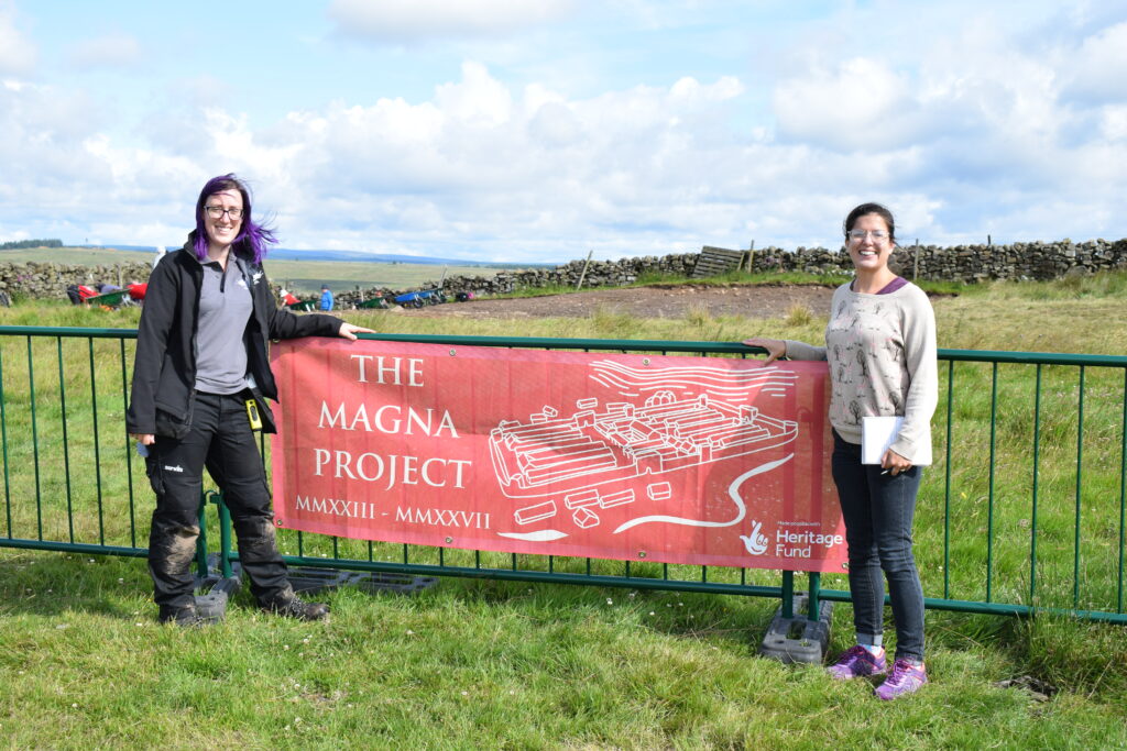 Two people standing next to a red banner that reads The Magna Project.