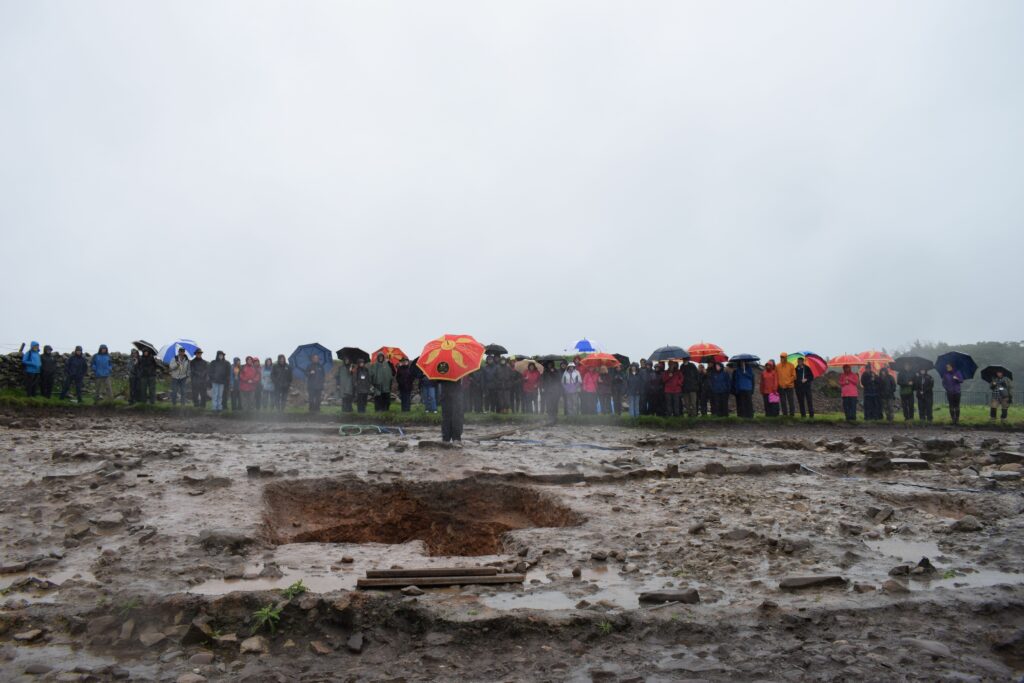 Landscape shot of large group pf people stood on the side of an archaeological trench. 