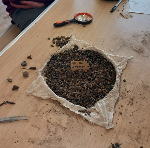 Image of a table with an open cheesecloth with dried soil inside. There are tweezers and a magnifying glass on the table too.