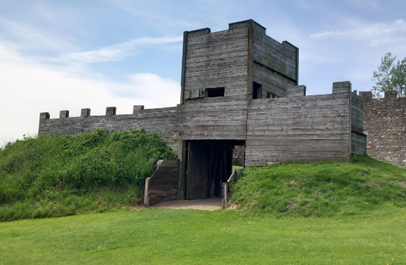 Image of a wooden replica of Hadrian's Wall set in a landscape of green grass.