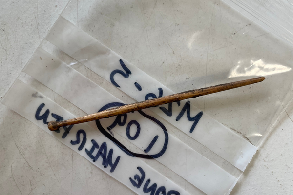 A slim ancient bone hairpin resting on a labelled archaeological finds bag.