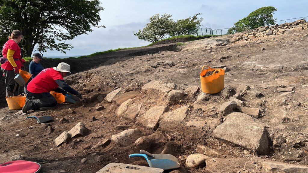 Group of three volunteers at Magna Roman Fort excavating a stone wall.