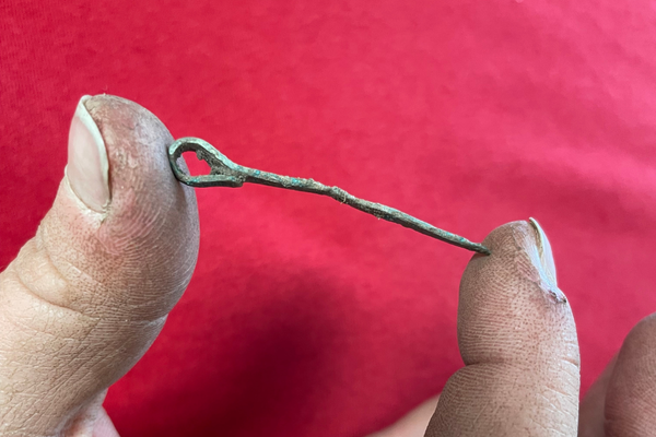 A hand holding a small ancient bronze pin with a looped head.