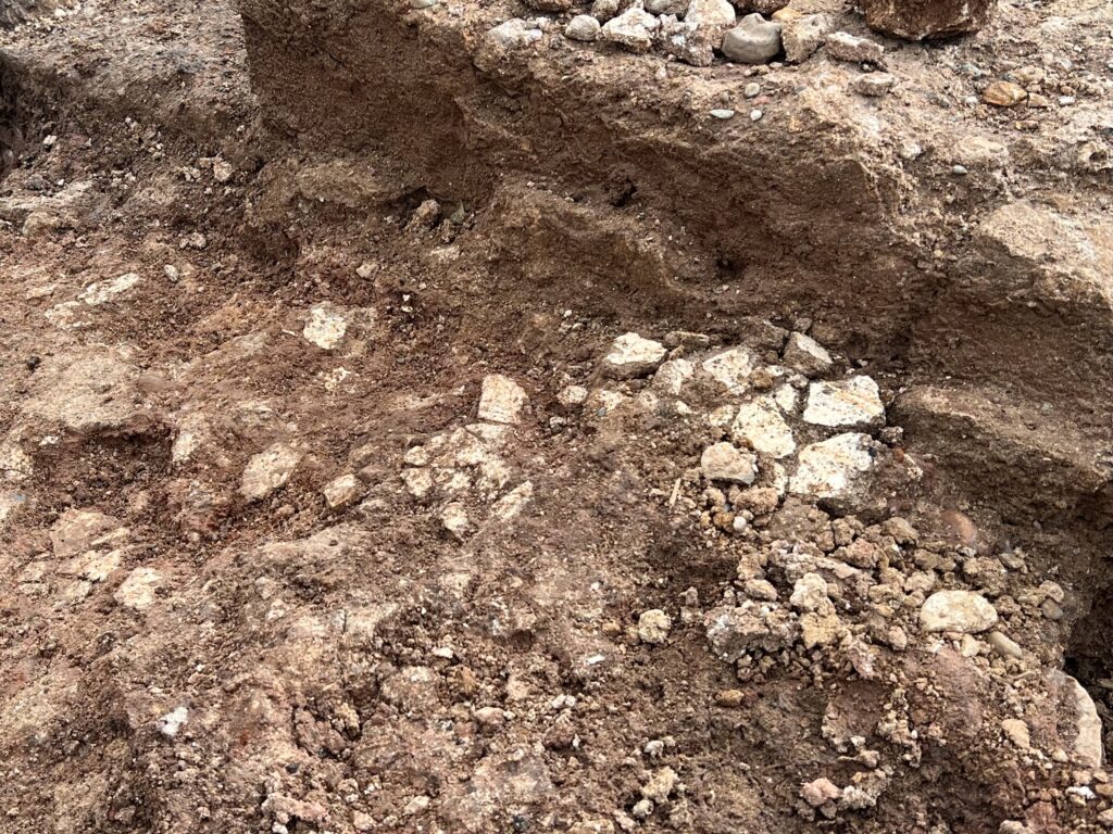 Close-up of an excavation trench floor showing contrasting soil layers and patches of painted plaster.